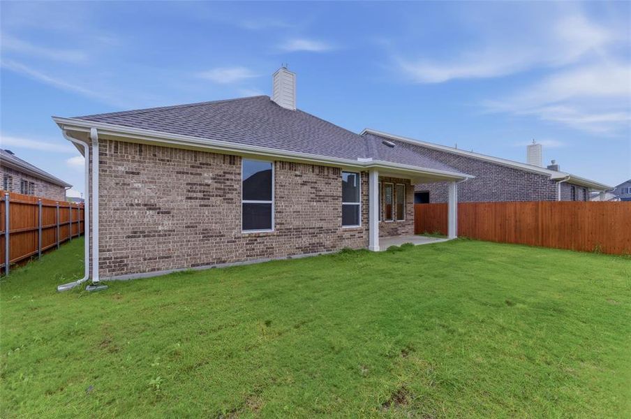 Expansive lawn featuring a covered patio, brick exterior, dark shingle roof, and wood privacy fencing