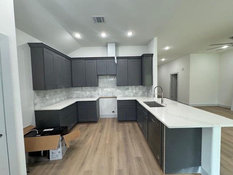 This is a spacious, modern kitchen featuring dark cabinetry, light countertops, a subway tile backsplash, and stainless steel appliances. It has recessed lighting and a large island, with wood-look flooring throughout.