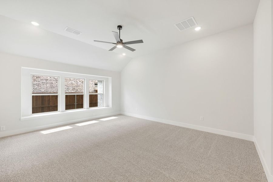 Empty bedroom with vaulted ceiling, ceiling fan, carpet flooring, and large window with natural light
