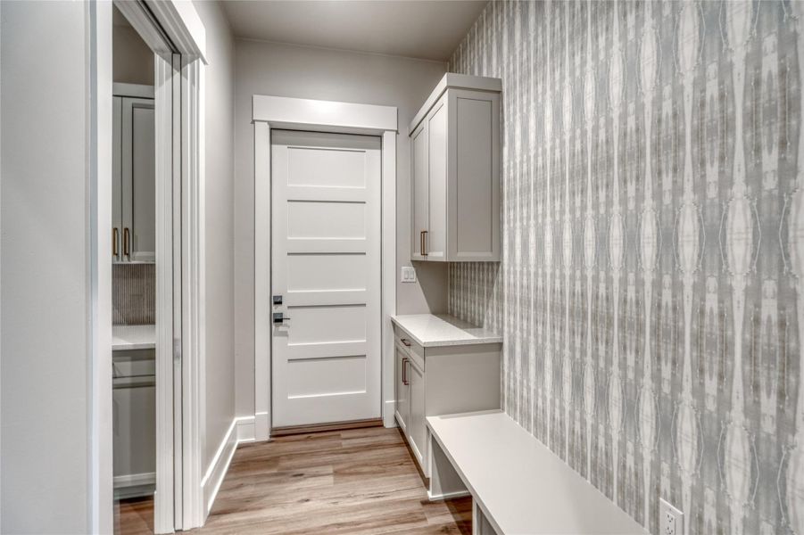 Mudroom featuring light wood-style floors, wallpapered walls, and baseboards