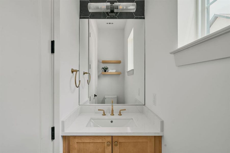 Bathroom vanity featuring a light wood-finish cabinet, white countertop with an integrated sink, and gold-finish faucet
