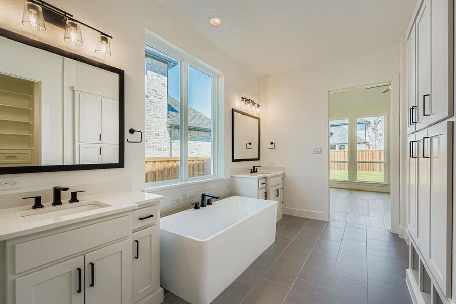 Bathroom featuring healthy amount of natural light, a freestanding tub, two vanities, dark tile patterned floors, and recessed lighting Bathroom featuring healthy amount of natural light, a freestanding tub, two vanities, dark tile patterned floors, and recessed lighting