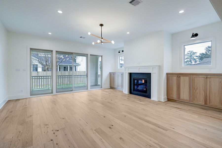 Sunlight streams into the living room through the large windows and sliding door, illuminating the natural tones. At the center of the room is a gas fireplace. *Previous Project*