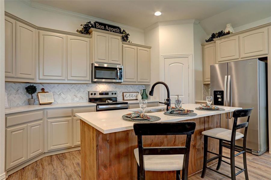 Kitchen with light hardwood / wood-style flooring, tasteful backsplash, ornamental molding, a kitchen island with sink, and appliances with stainless steel finishes