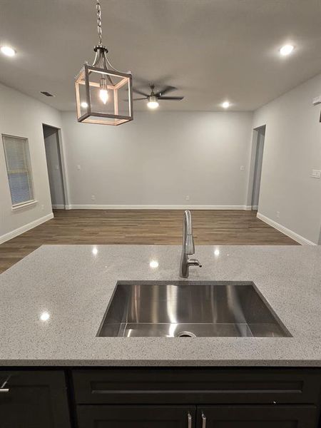 Kitchen with light stone countertops, ceiling fan, dark wood-type flooring, sink, and hanging light fixtures