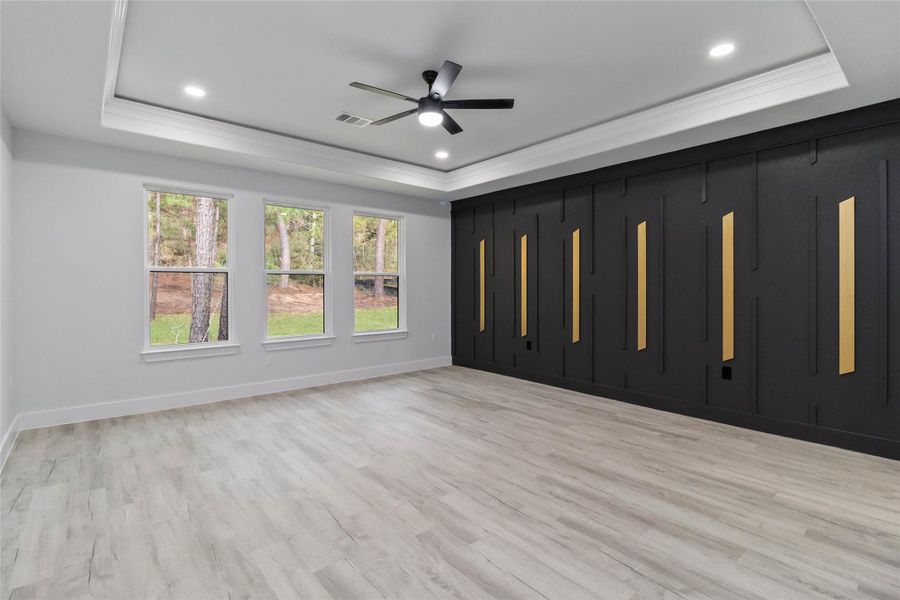Unfurnished bedroom featuring a tray ceiling, light wood finished floors, a ceiling fan, recessed lighting, and ornamental molding