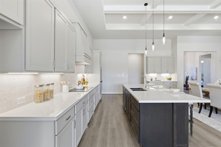 Kitchen with two tone cabinetry, hanging light fixtures, light wood-style flooring, an island with sink, and beamed ceiling