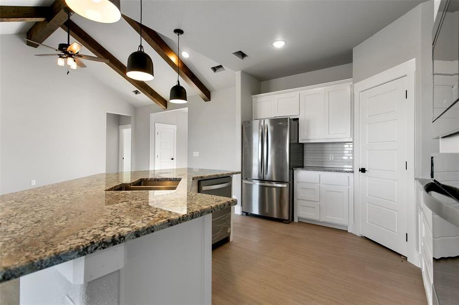 Kitchen with appliances with stainless steel finishes, light wood-type flooring, decorative light fixtures, and white cabinetry