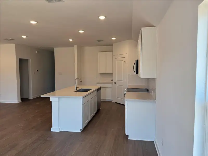 Kitchen with a kitchen island with sink, dark wood-style flooring, appliances with stainless steel finishes, recessed lighting, and white cabinets Kitchen with a kitchen island with sink, dark wood-style flooring, appliances with stainless steel finishes, recessed lighting, and white cabinets