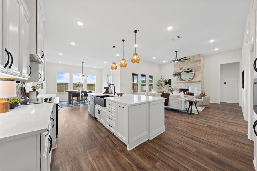 Kitchen featuring white cabinetry, a stone fireplace, dark wood-style flooring, open floor plan, and pendant lighting Kitchen featuring white cabinetry, a stone fireplace, dark wood-style flooring, open floor plan, and pendant lighting
