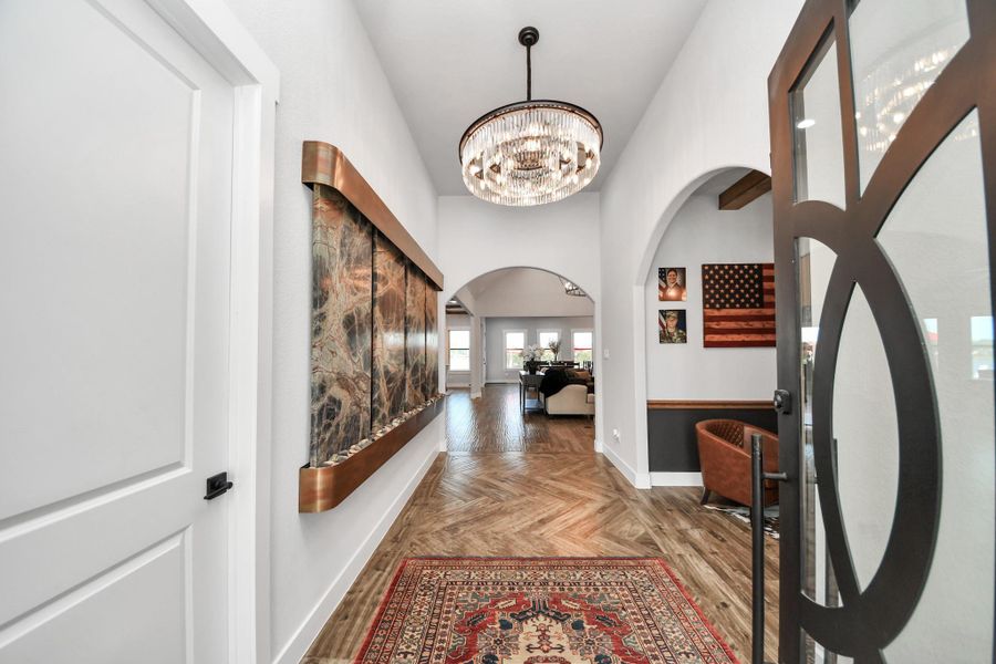 Elegant entryway featuring a stunning chandelier, artistic wall decor, and rich wood flooring leading to a spacious living area.