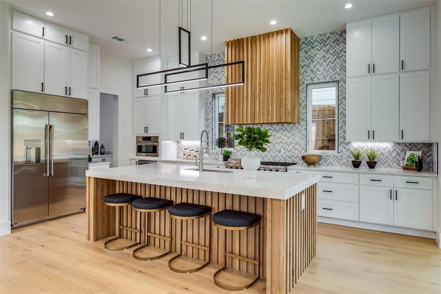 Kitchen featuring a kitchen island with sink, appliances with stainless steel finishes, decorative backsplash, and light hardwood / wood-style floors