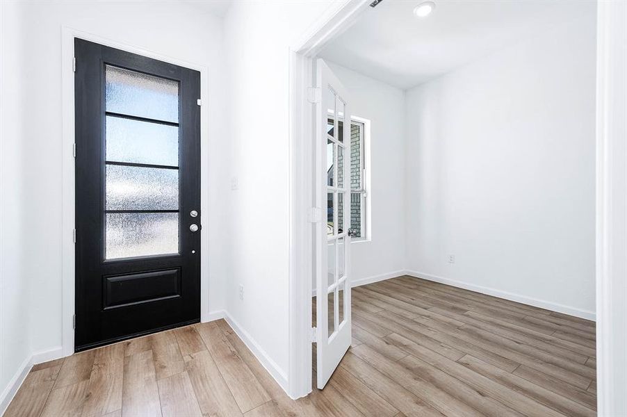 A stylish entryway featuring a sleek glass-paneled door, leading to a cozy home office with beautiful French doors and natural light.