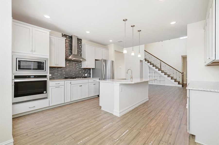 Kitchen with white cabinetry, pendant lighting, wall chimney exhaust hood, and stainless steel appliances