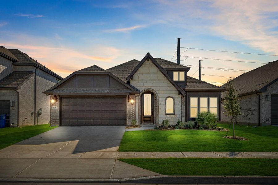 Single-story home with stone and brick exterior, two-car garage, arched entry, and manicured lawn at dusk.
