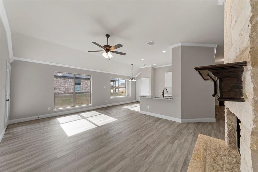 Unfurnished living room featuring light wood-type flooring, ceiling fan with notable chandelier, crown molding, sink, and a fireplace