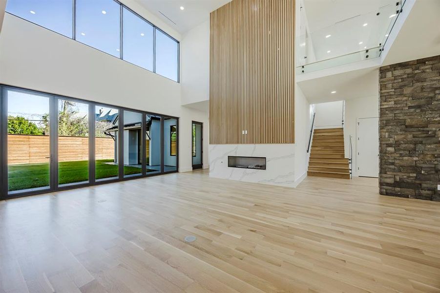 Unfurnished living room with light wood-style floors, a high ceiling, a high end fireplace, recessed lighting, and stairway Unfurnished living room with light wood-style floors, a high ceiling, a high end fireplace, recessed lighting, and stairway