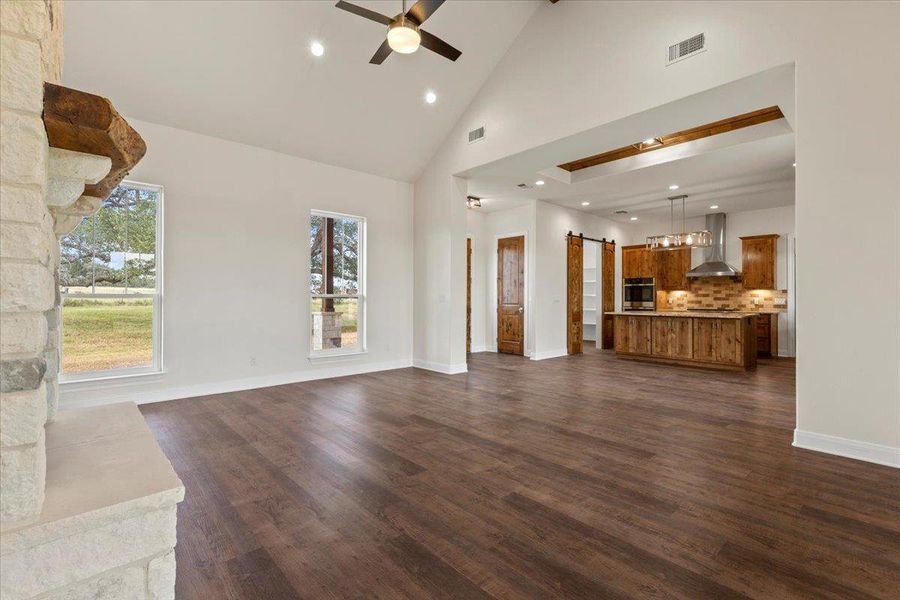 Unfurnished living room with high vaulted ceiling, ceiling fan, recessed lighting, dark wood-style flooring, and a barn door