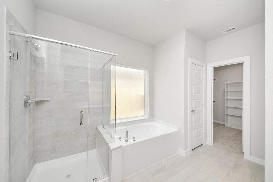 Indulge in a spa-like retreat within the confines of this primary bathroom. Delight in a spacious walk-in shower enveloped in stylish tile surround and unwind in a separate garden tub adorned with custom detailing. Sample photo of completed home with similar floor plan. Actual colors and selections may vary.