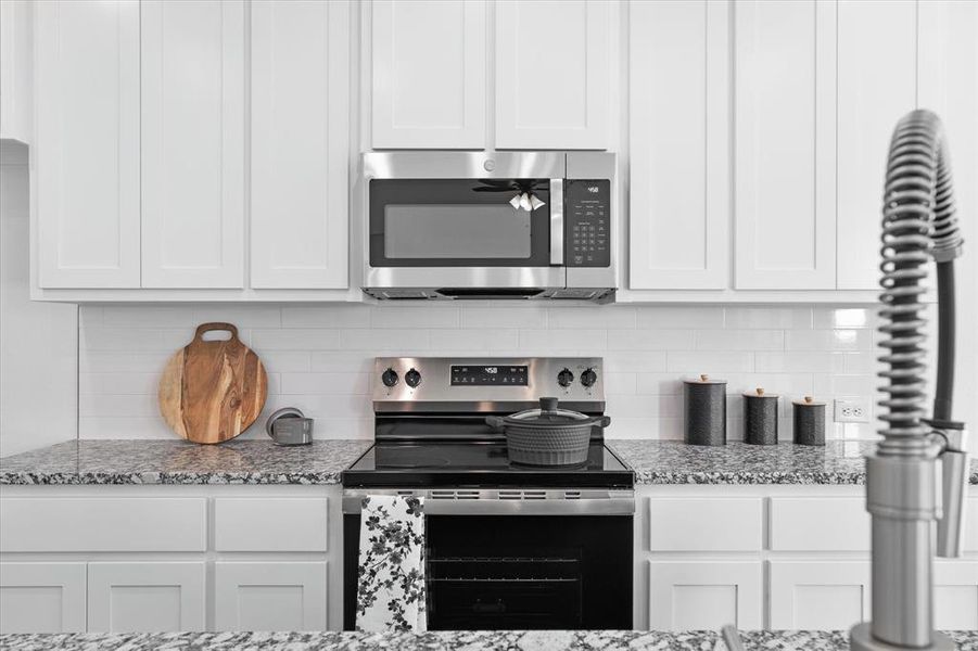 Kitchen with light stone counters, white cabinets, appliances with stainless steel finishes, and decorative backsplash