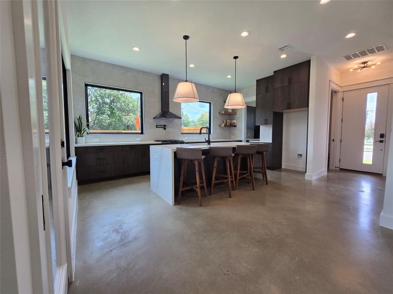 Full wall of backsplash tile surrounding the huge windows, range hood, pot filler, reclaimed wood accent shelving, waterfall island countertop.