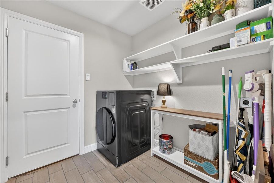 Utility room featuring wood-finish flooring, two white wall-mounted shelves, and a built-in vent