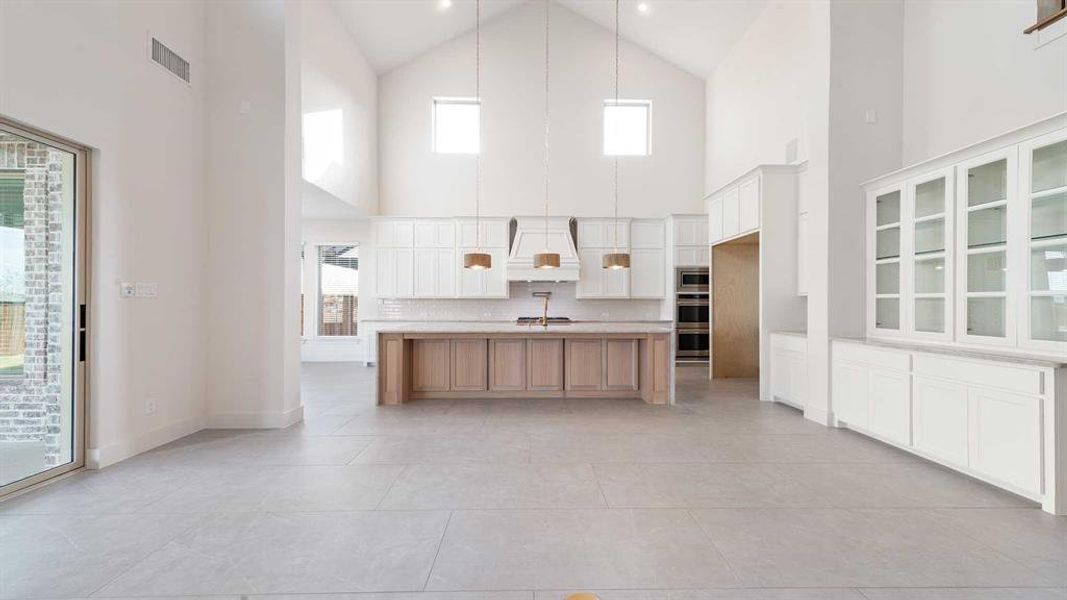 Kitchen featuring white cabinets, a center island with sink, high vaulted ceiling, and a wealth of natural light