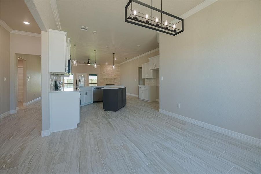 Kitchen with a center island, white cabinetry, open floor plan, ornamental molding, and hanging light fixtures