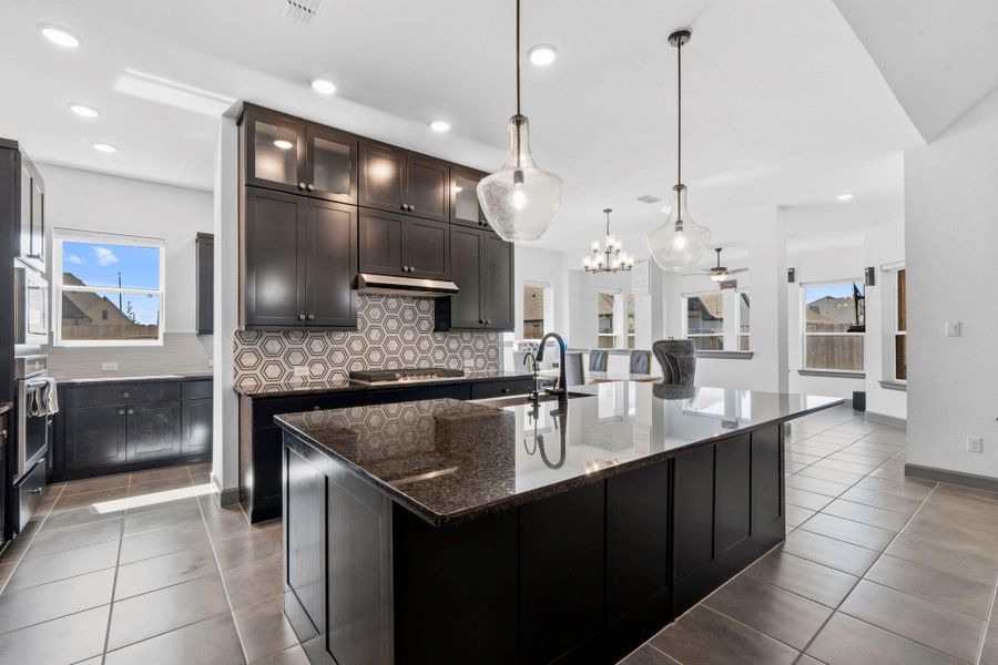Chef-inspired kitchen featuring a large island, granite countertops, custom cabinetry, and stylish designer backsplash.