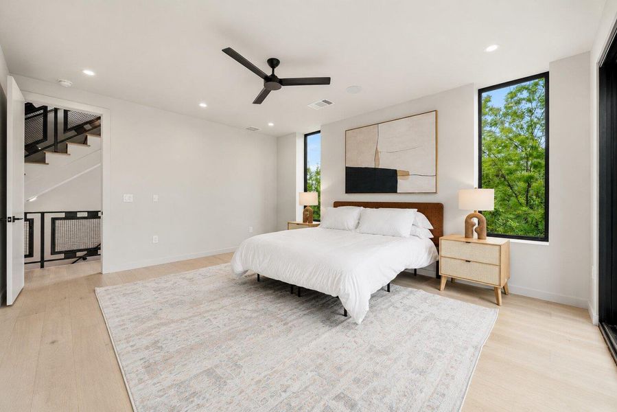 A well-lit bedroom with blonde hardwood floors, offering tree views from generous windows.
