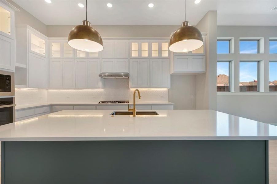 Kitchen featuring glass fronted cabinets, an island with sink, and white cabinetry Kitchen featuring glass fronted cabinets, an island with sink, and white cabinetry
