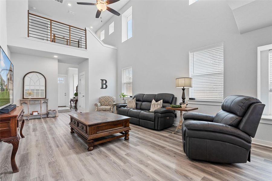 Living room with a ceiling fan, light wood-type flooring, recessed lighting, a towering ceiling, and baseboards Living room with a ceiling fan, light wood-type flooring, recessed lighting, a towering ceiling, and baseboards