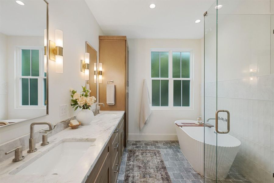 Indulge in a spa-like retreat with this well-appointed primary bathroom, featuring dual vanities, a glass-enclosed shower, and a soaking tub.