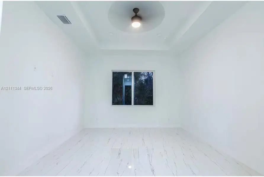 Interior room featuring a tray ceiling with a central integrated lighting fixture, white stone-patterned flooring, and a sliding window Interior room featuring a tray ceiling with a central integrated lighting fixture, white stone-patterned flooring, and a sliding window