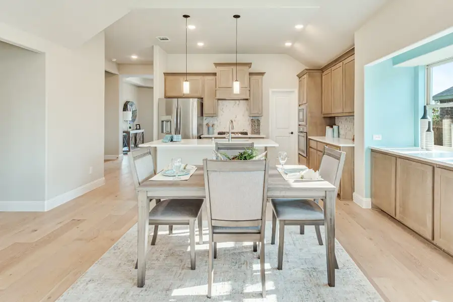 Open dining area with gray table and chairs flowing into kitchen with wood cabinets and center island