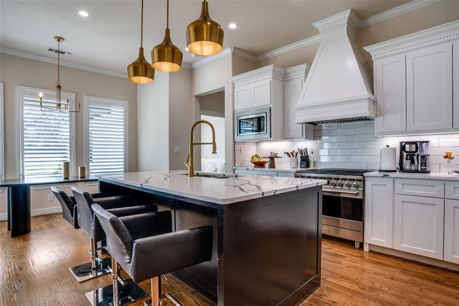 Kitchen with custom exhaust hood, a kitchen island with sink, sink, hanging light fixtures, and stainless steel appliances