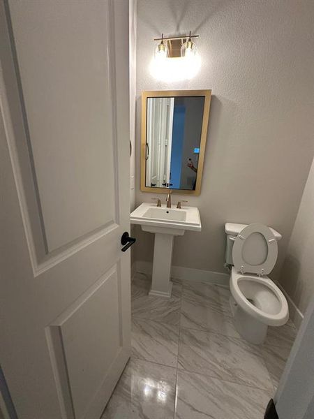 Half bathroom featuring light marble finish floors and a textured wall Half bathroom featuring light marble finish floors and a textured wall