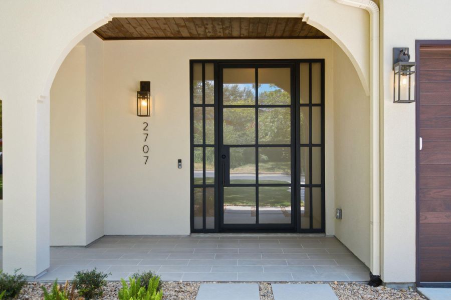 An arched entry porch showcases a modern glass door and wood-paneled ceiling details.