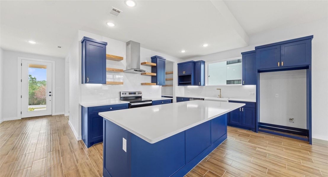 Kitchen with blue cabinetry, light wood finished floors, stainless steel electric stove, open shelves, and recessed lighting