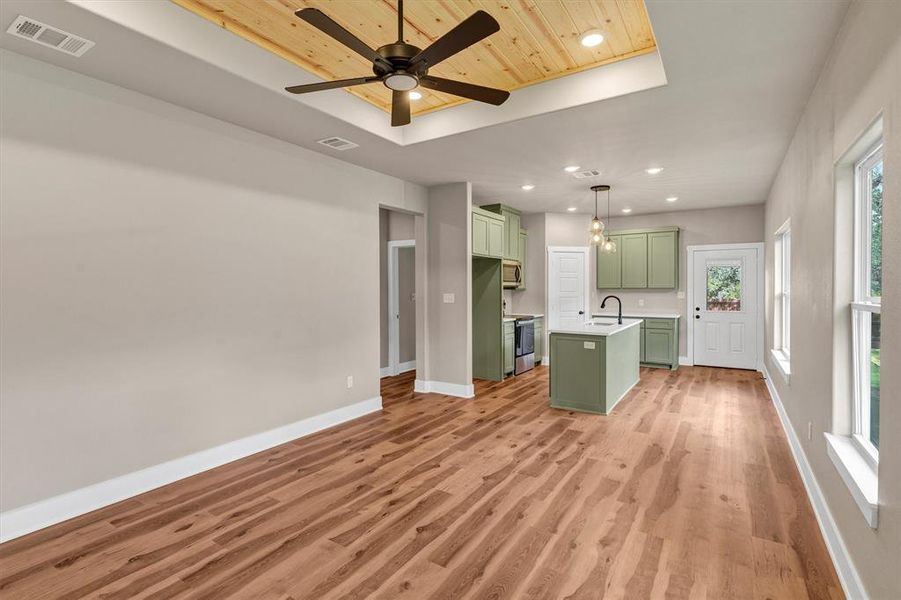 Kitchen featuring green cabinetry, recessed lighting, a raised ceiling, light wood-style flooring, and decorative light fixtures Kitchen featuring green cabinetry, recessed lighting, a raised ceiling, light wood-style flooring, and decorative light fixtures