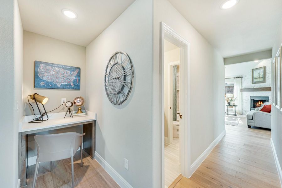 Hallway with built-in desk nook, hardwood floors, and view into living room with fireplace
