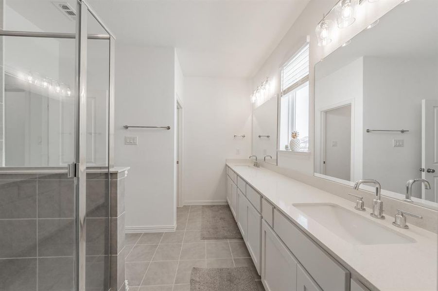 Full bath featuring double vanity, light tile patterned floors, and a shower stall