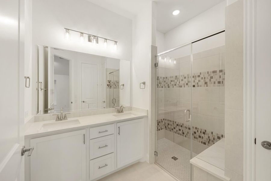 Bathroom with double sink vanity, white cabinets, and glass-enclosed tile shower with mosaic accent strip