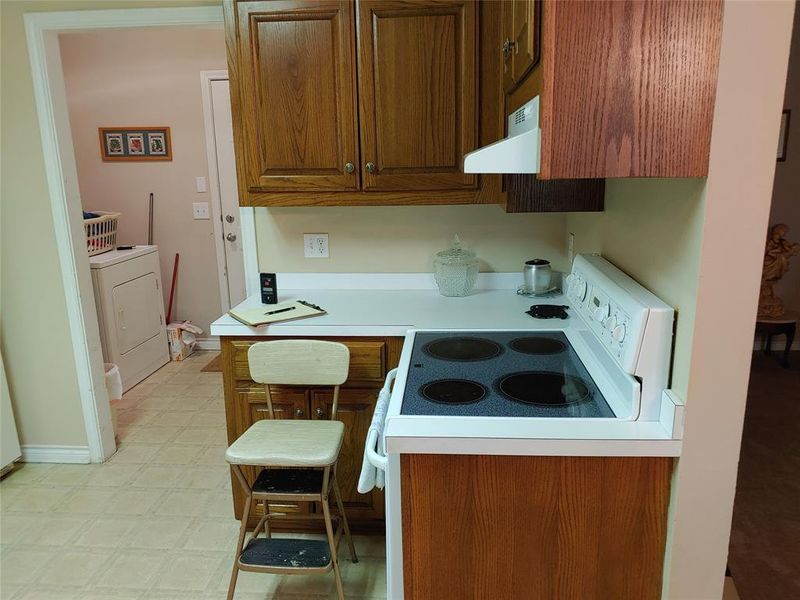 Kitchen featuring wood-finish cabinetry, white countertops, and a built-in electric range with exhaust hood