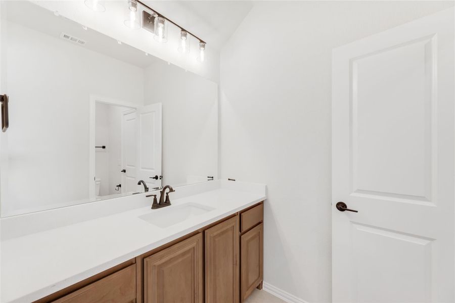 Bathroom vanity with wood cabinets, white countertop, single sink, large mirror, and overhead lighting fixture. Bathroom vanity with wood cabinets, white countertop, single sink, large mirror, and overhead lighting fixture.