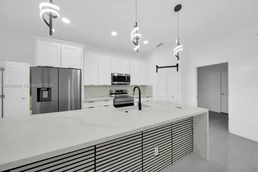 Kitchen featuring white cabinetry, an expansive island with stone-finish countertops, stainless steel appliances, matte black hardware, and contemporary spiral pendant lighting