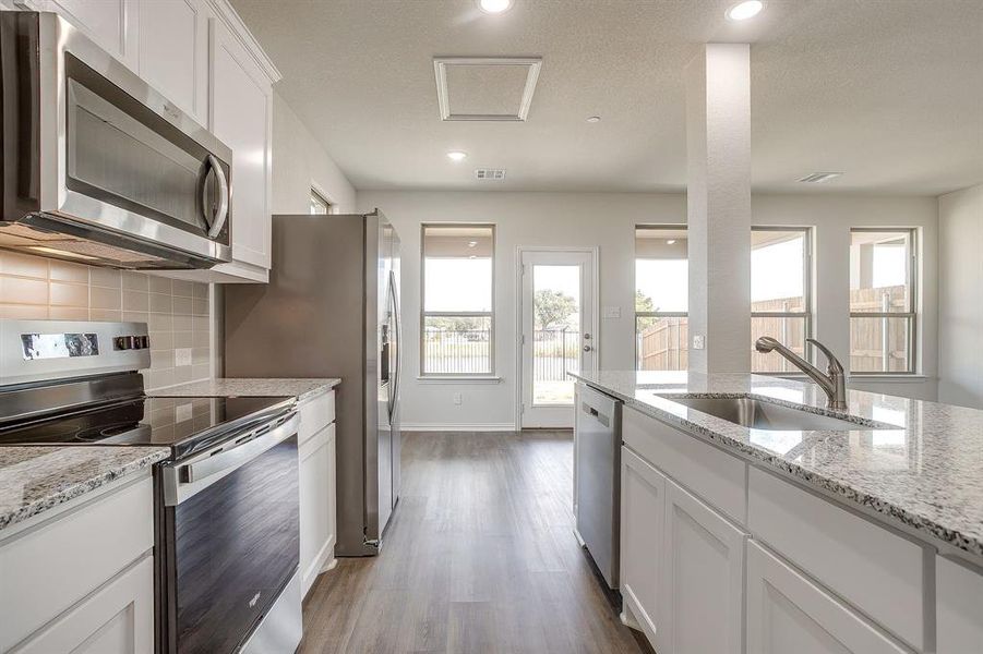 Kitchen featuring stainless steel appliances, white cabinets, light stone counters, dark wood-type flooring, and decorative backsplash