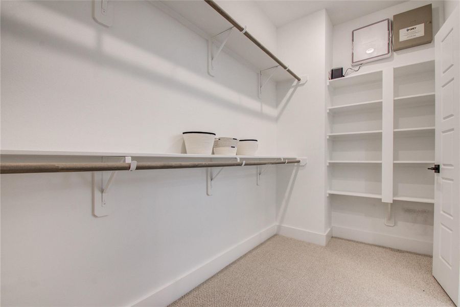 A spacious and well-organized primary walk-in closet designed for maximum storage and convenience. The closet features custom-built shelving and hanging rods to accommodate a variety of clothing and accessories. Soft, recessed lighting illuminates the space, creating a bright and inviting atmosphere A spacious and well-organized primary walk-in closet designed for maximum storage and convenience. The closet features custom-built shelving and hanging rods to accommodate a variety of clothing and accessories. Soft, recessed lighting illuminates the space, creating a bright and inviting atmosphere