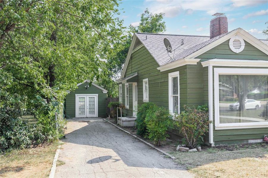 View of front of property featuring a shingled roof, a chimney, an outbuilding, and french doors View of front of property featuring a shingled roof, a chimney, an outbuilding, and french doors