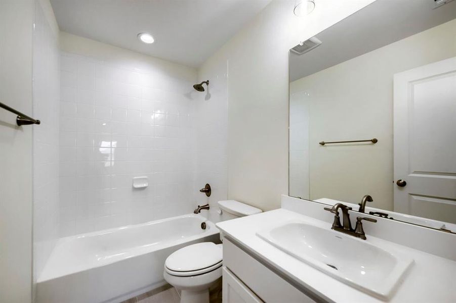 Bright bathroom featuring a white tub and shower combination with subway tile surround, single vanity with integrated sink, and bronze fixtures Bright bathroom featuring a white tub and shower combination with subway tile surround, single vanity with integrated sink, and bronze fixtures
